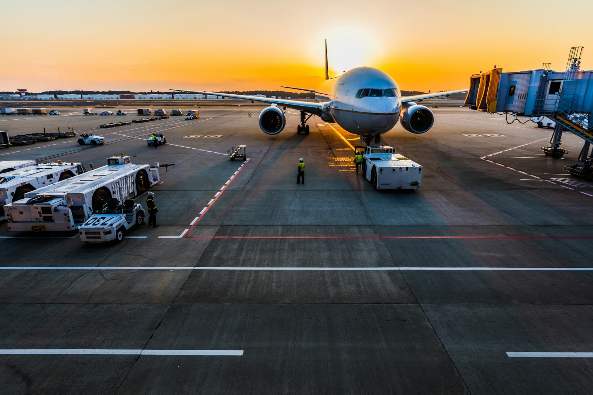 A jet at the gate on the apron at sunset, ground crew alongside