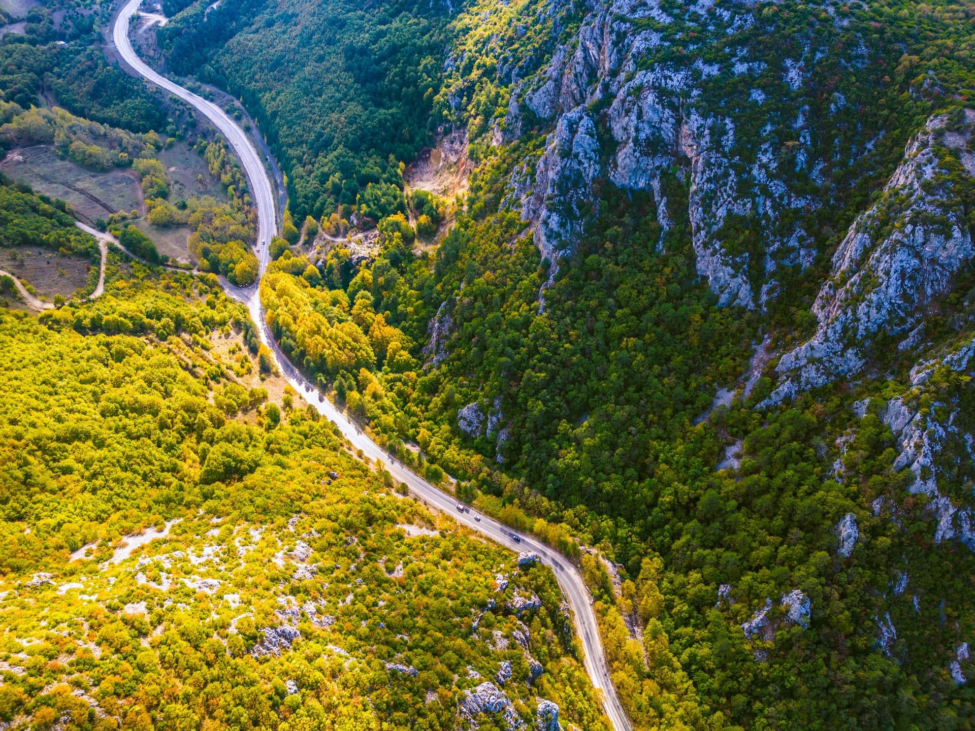 A rental car on a winding canyon road through green Montenegrin mountains, from above