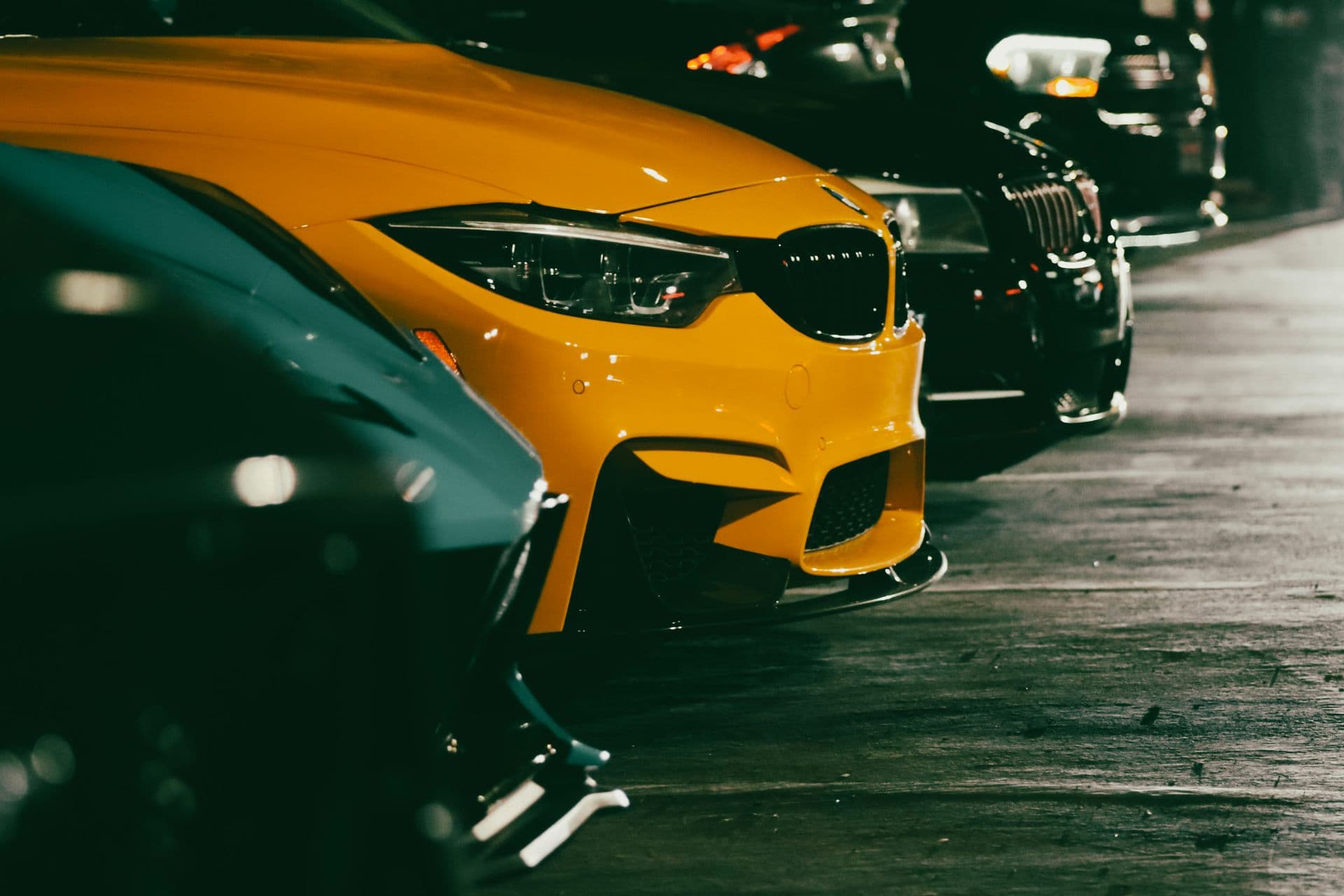 A lineup of cars parked at night, a yellow coupe at the front