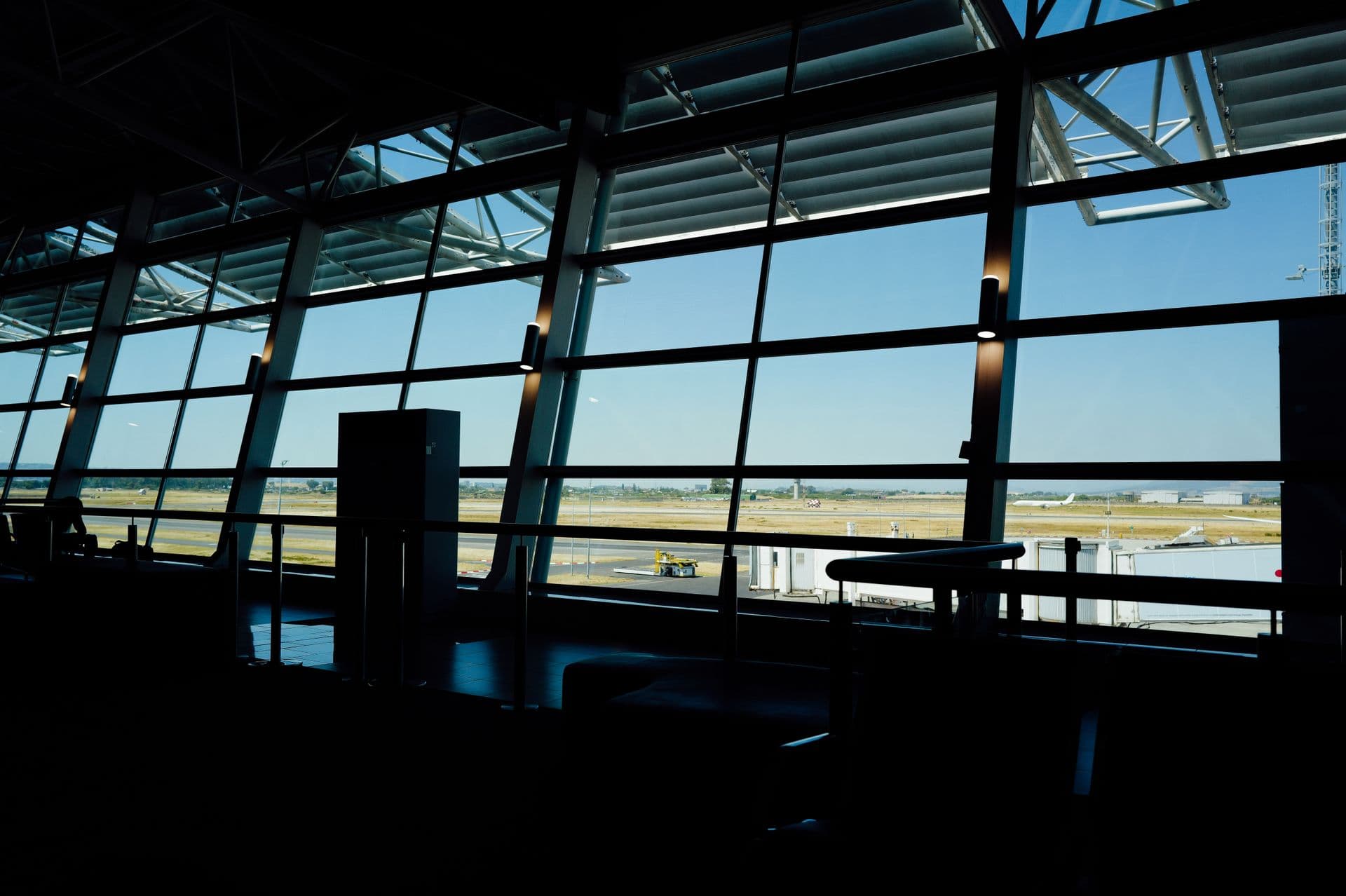 The apron and runway seen through a terminal's glass wall, a jet in the distance