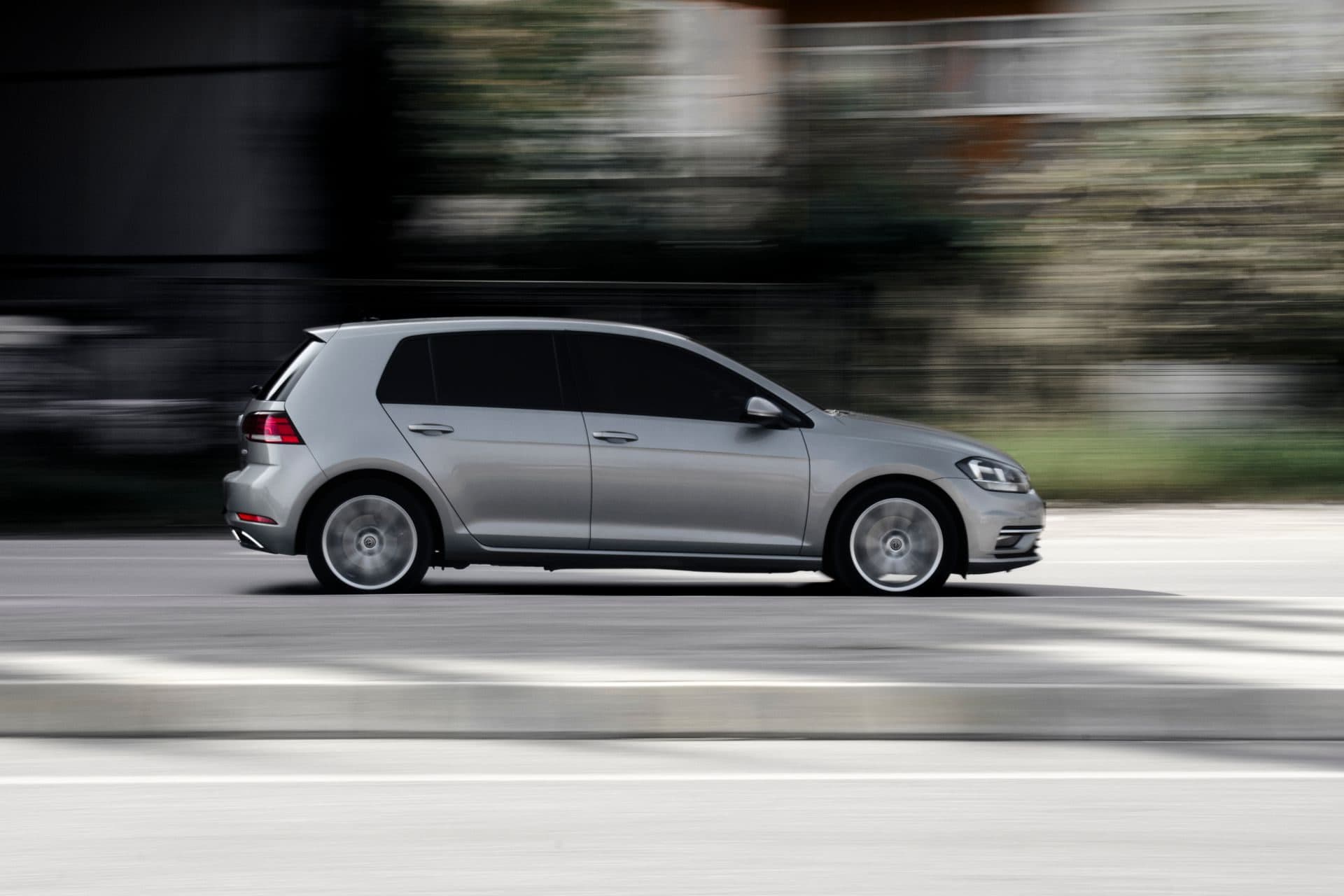 A silver VW Golf hatchback driving fast on the road, panned