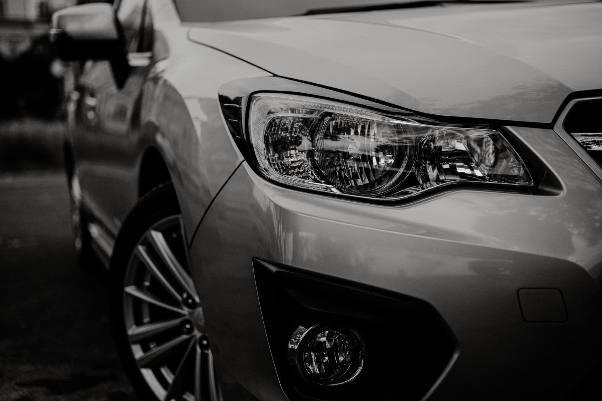 A car's headlight and front wing in close-up, black and white