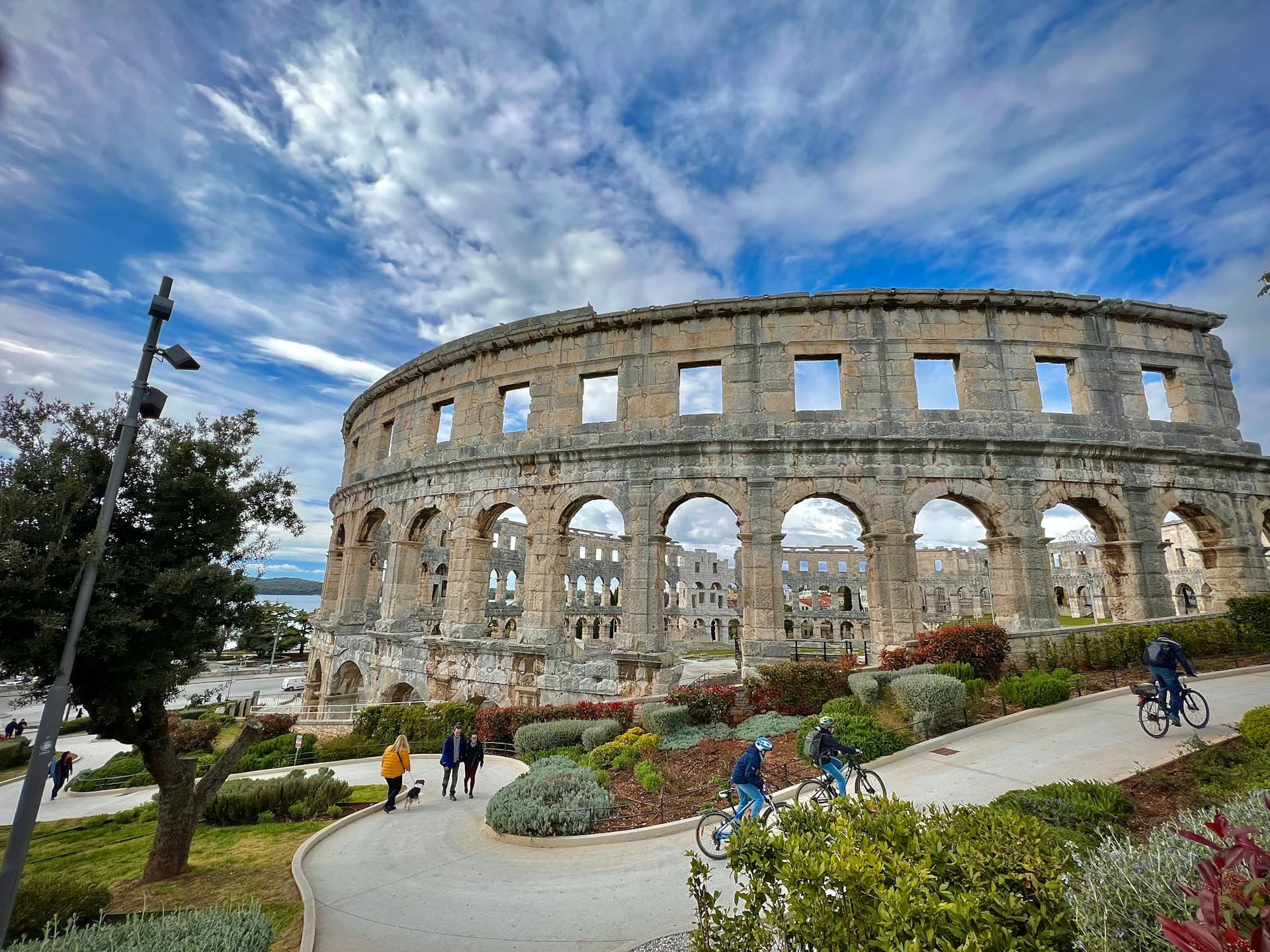 Cyclists on the path past Pula's Roman arena under a big sky