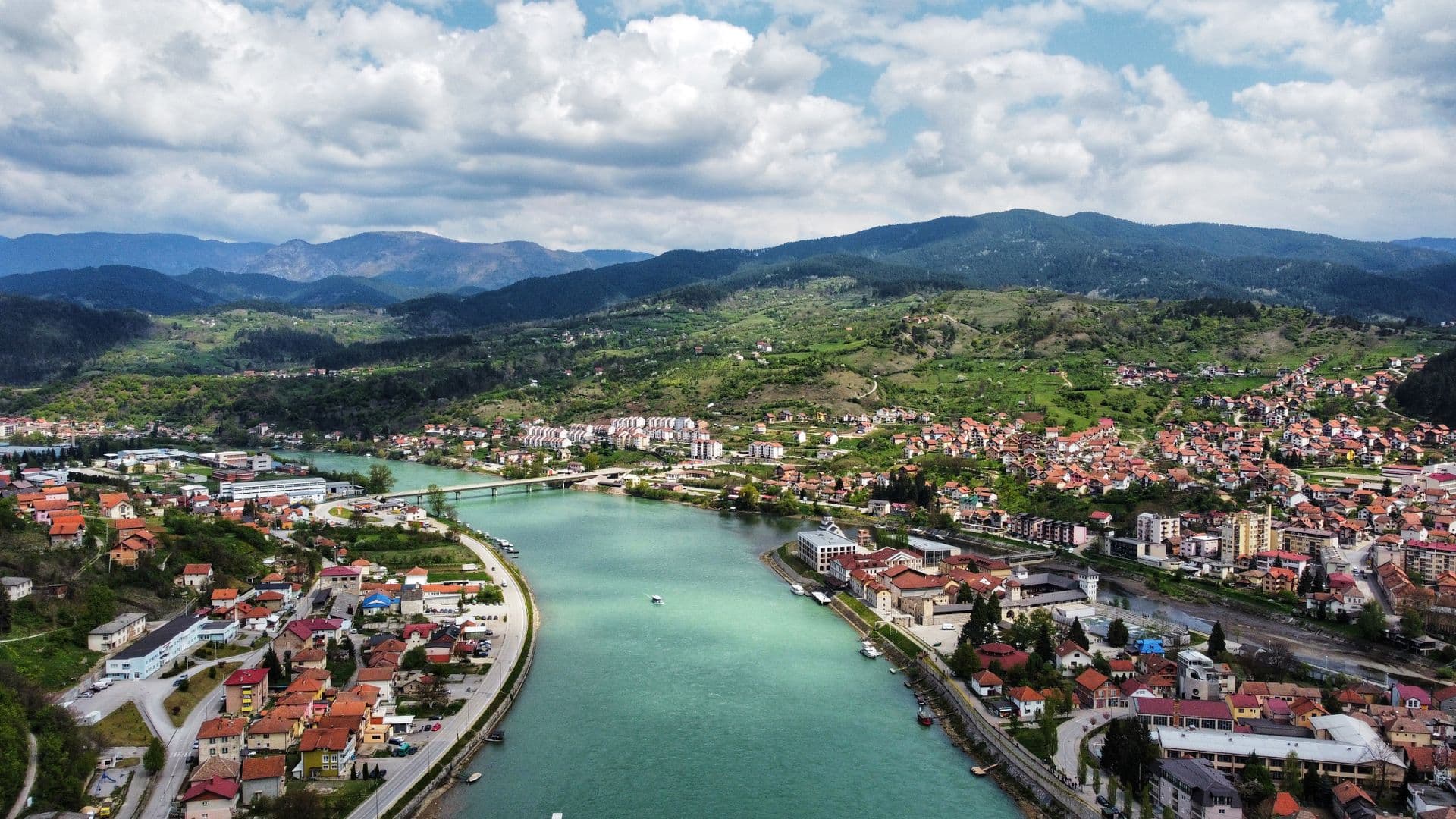 A river winding between a red-roofed town and green mountains, from the air